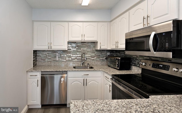 kitchen with light stone countertops, appliances with stainless steel finishes, sink, and white cabinets