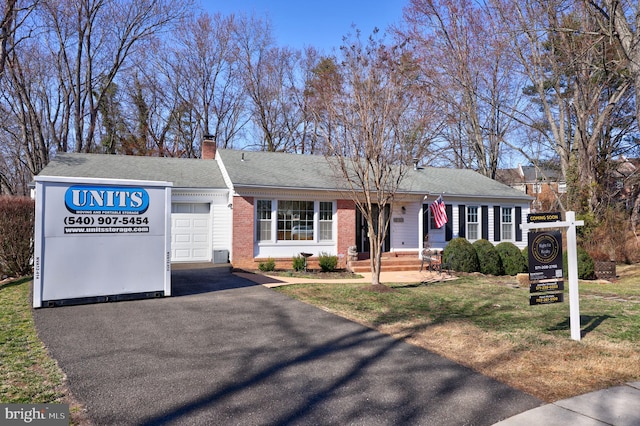 single story home with brick siding, a front lawn, aphalt driveway, a chimney, and an attached garage