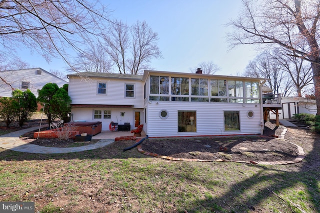 rear view of property with a chimney, a hot tub, a patio, and a sunroom