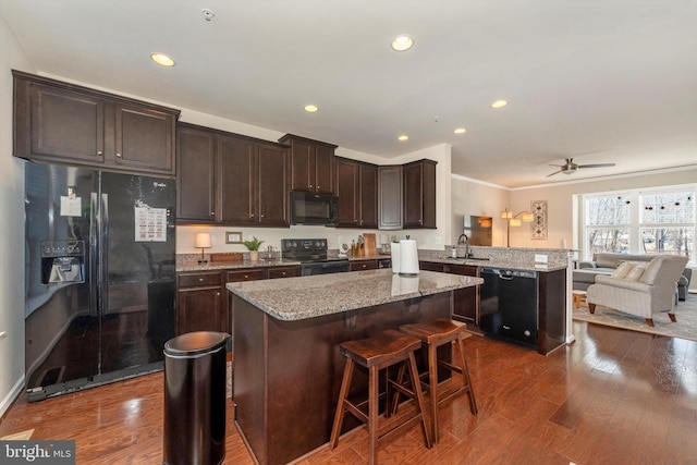 kitchen with a breakfast bar, dark hardwood / wood-style floors, black appliances, sink, and kitchen peninsula