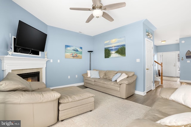 living area featuring ceiling fan, wood finished floors, baseboards, stairs, and a glass covered fireplace