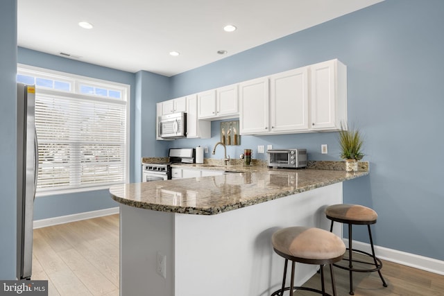 kitchen featuring a breakfast bar area, appliances with stainless steel finishes, light stone counters, a peninsula, and light wood-style floors