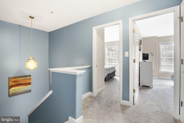 corridor with baseboards, light carpet, and an upstairs landing