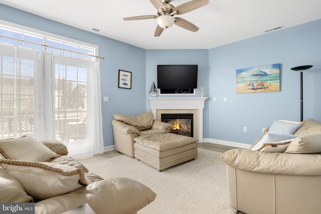 living area featuring a ceiling fan, a glass covered fireplace, visible vents, and light wood-style floors