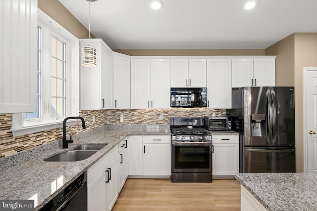 kitchen featuring sink, white cabinets, hanging light fixtures, light stone counters, and black appliances