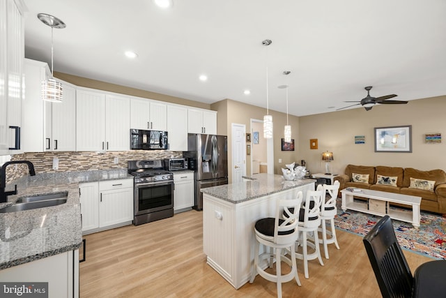 kitchen with sink, white cabinetry, a center island, hanging light fixtures, and appliances with stainless steel finishes