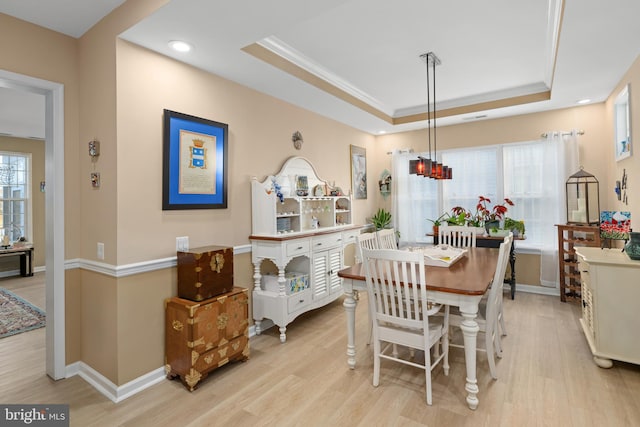 dining space featuring plenty of natural light, ornamental molding, a raised ceiling, and light wood-type flooring