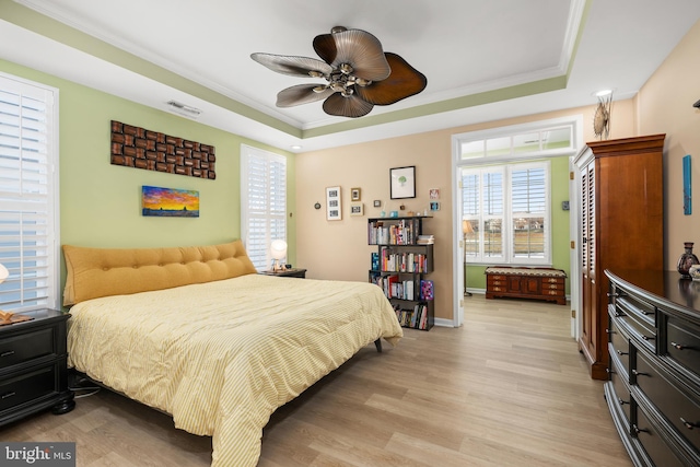 bedroom featuring ornamental molding, light hardwood / wood-style flooring, ceiling fan, and a tray ceiling