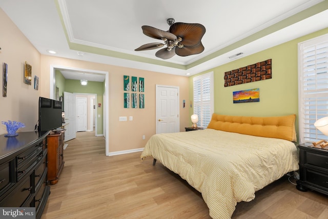 bedroom with ceiling fan, ornamental molding, a raised ceiling, and light hardwood / wood-style floors