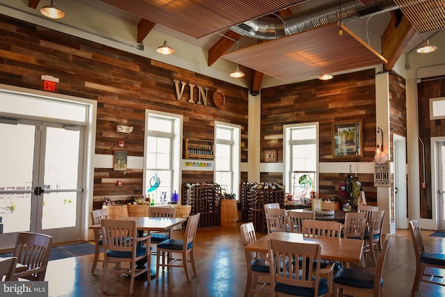 dining area with beamed ceiling, a high ceiling, wooden walls, and french doors