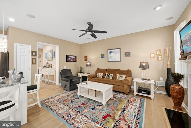 living room with a fireplace, ceiling fan, and light hardwood / wood-style flooring