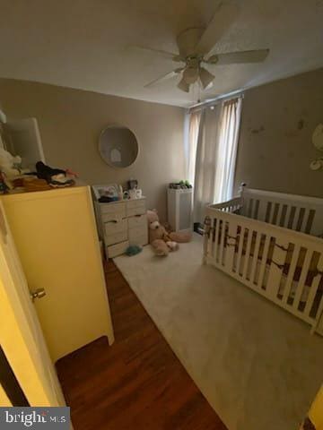 bedroom featuring dark wood-type flooring, a nursery area, and ceiling fan