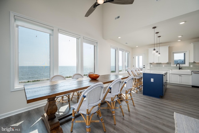 dining room with sink, dark wood-type flooring, ceiling fan, and a water view