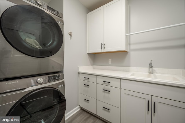 washroom featuring stacked washer and dryer, wood-type flooring, sink, and cabinets