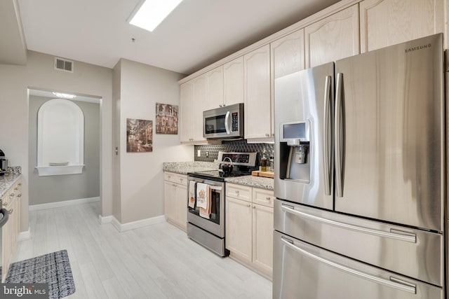 kitchen with appliances with stainless steel finishes, decorative backsplash, light stone counters, and light hardwood / wood-style floors