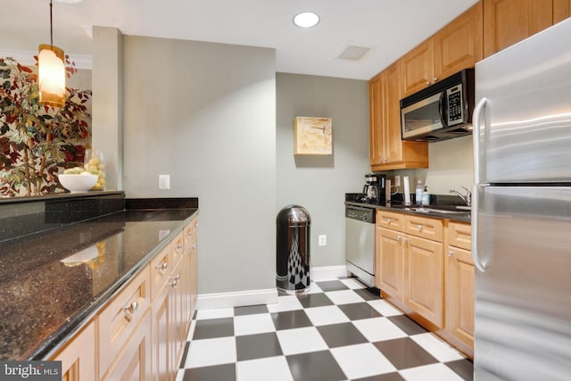 kitchen featuring light brown cabinetry, sink, dark stone counters, hanging light fixtures, and stainless steel appliances