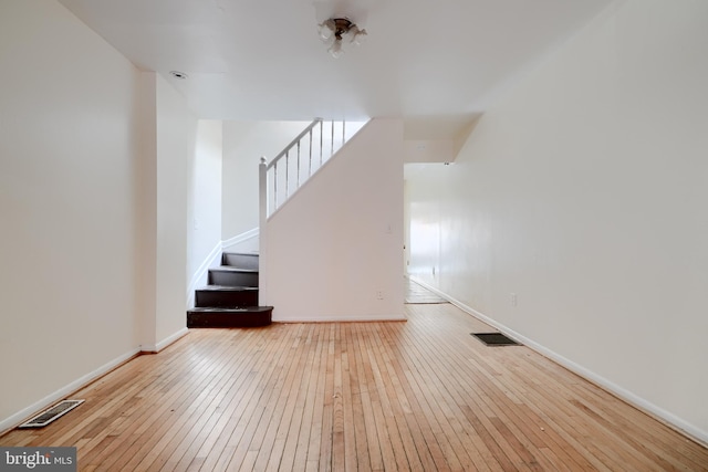 unfurnished living room featuring baseboards, stairway, visible vents, and light wood-style floors