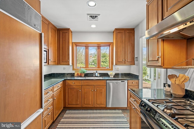 kitchen with sink, dark stone countertops, stainless steel dishwasher, gas range, and paneled refrigerator