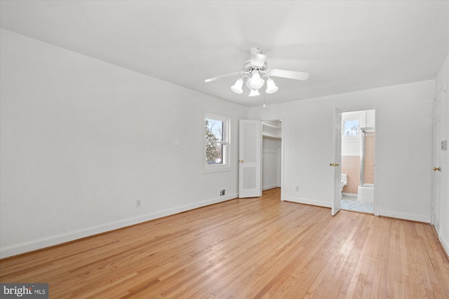 unfurnished bedroom featuring ensuite bathroom, a walk in closet, light wood-type flooring, a closet, and ceiling fan