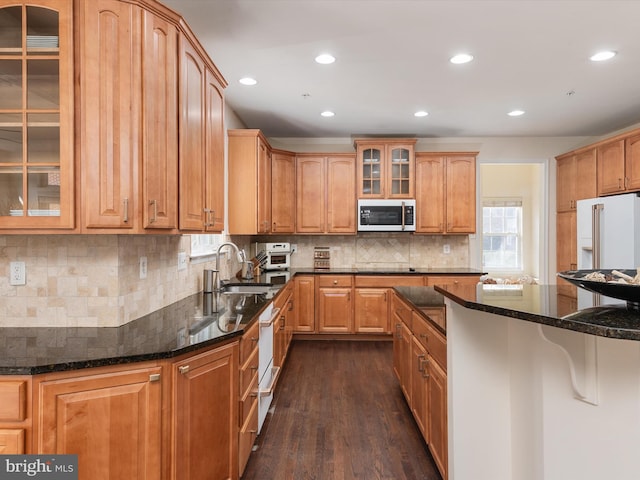 kitchen with white appliances, dark stone counters, dark hardwood / wood-style floors, and sink