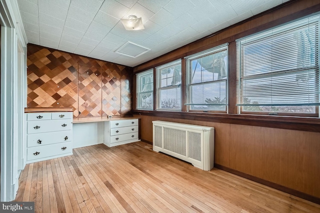 interior space featuring radiator, built in desk, light hardwood / wood-style floors, and wood walls