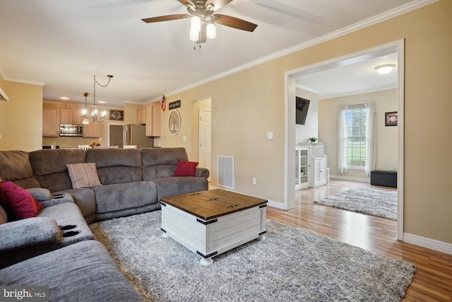 living room with ceiling fan with notable chandelier, wood-type flooring, and ornamental molding