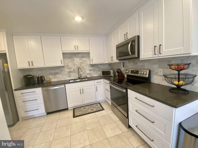 kitchen with stainless steel appliances, dark countertops, backsplash, white cabinetry, and a sink