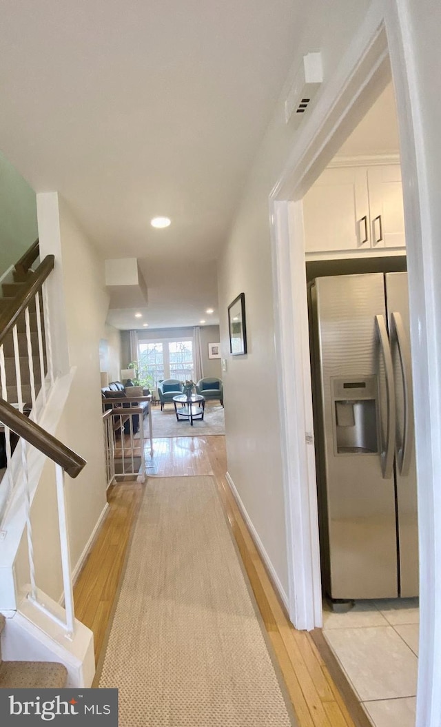 hallway with light wood-style floors, stairway, and baseboards