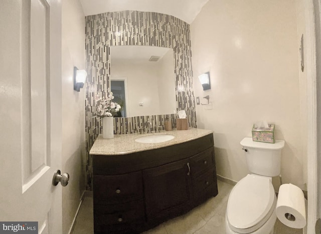 bathroom featuring tile patterned flooring, toilet, vanity, baseboards, and backsplash