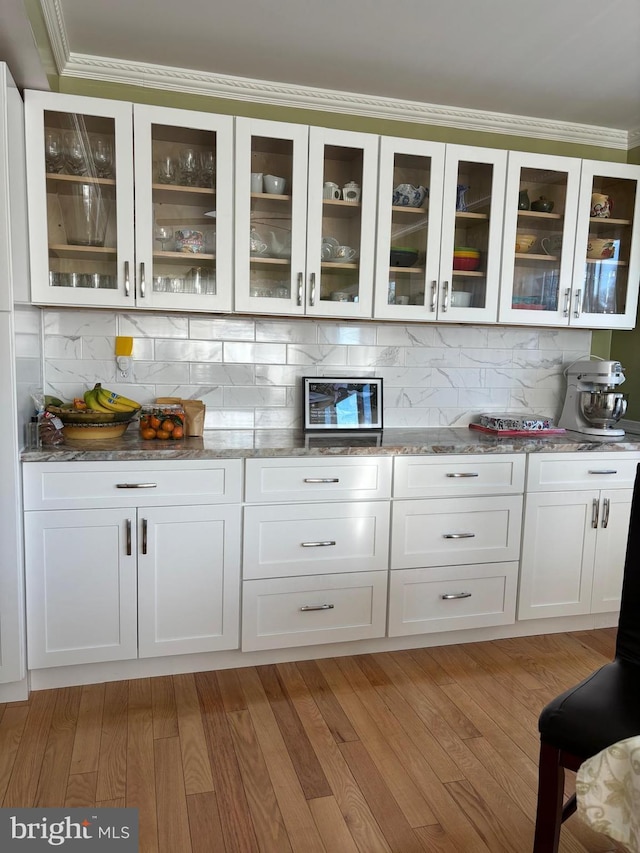 bar with light hardwood / wood-style flooring, white cabinets, dark stone counters, and decorative backsplash