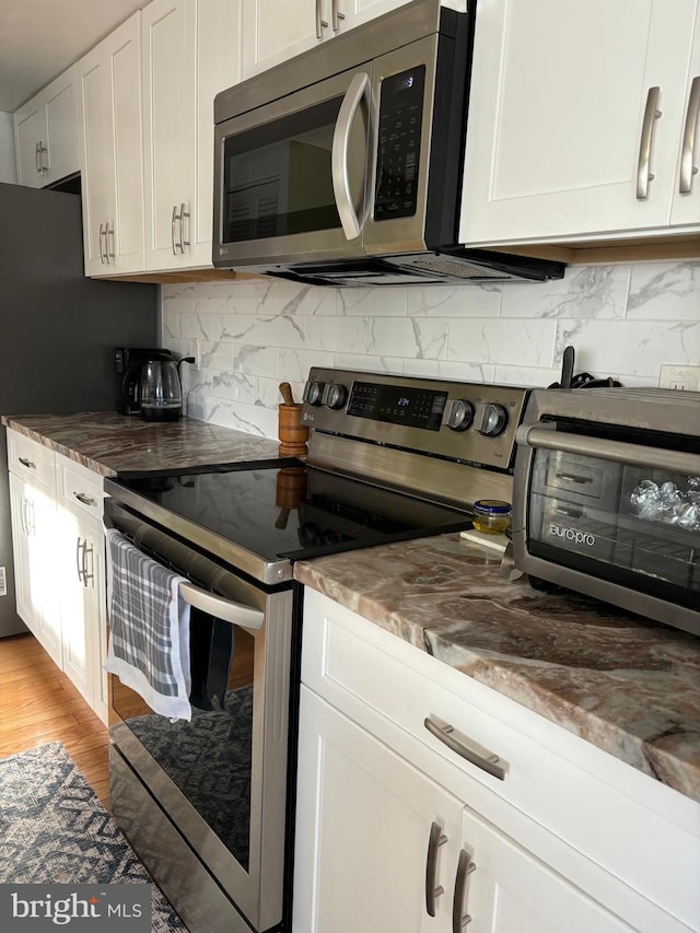 kitchen featuring appliances with stainless steel finishes, white cabinets, light hardwood / wood-style floors, and decorative backsplash