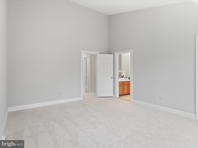 unfurnished bedroom featuring light colored carpet, ensuite bath, and a high ceiling