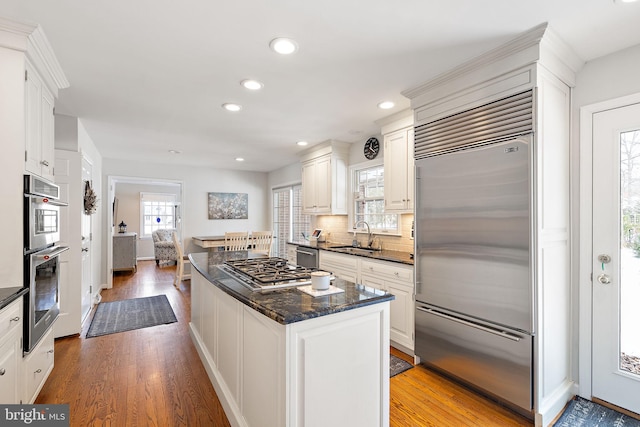 kitchen with sink, light hardwood / wood-style flooring, appliances with stainless steel finishes, decorative backsplash, and white cabinets