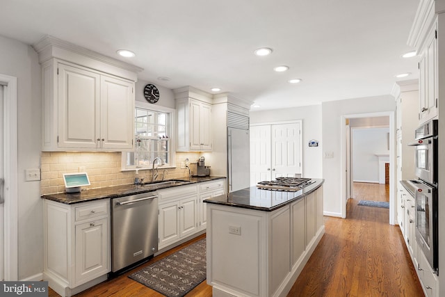 kitchen with dark wood-type flooring, appliances with stainless steel finishes, white cabinetry, a center island, and tasteful backsplash