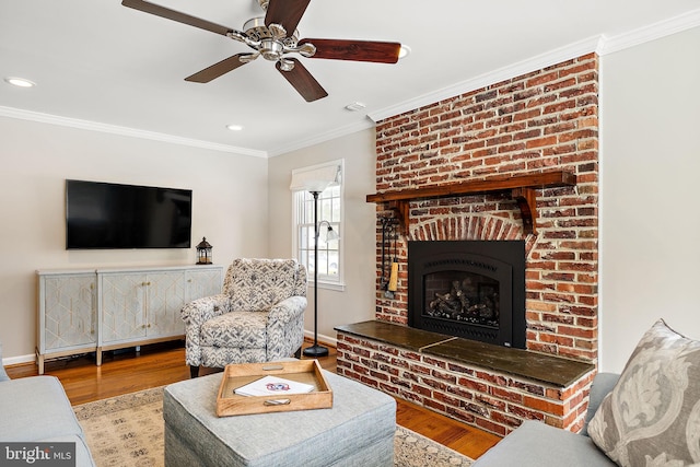 living room featuring hardwood / wood-style floors, crown molding, a fireplace, and ceiling fan