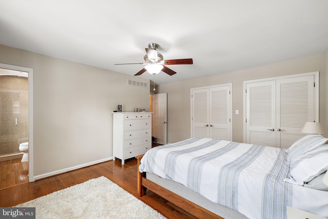 bedroom with connected bathroom, dark hardwood / wood-style floors, two closets, and ceiling fan