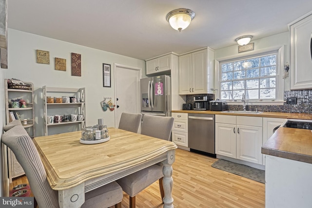 kitchen featuring sink, white cabinets, stainless steel appliances, light hardwood / wood-style floors, and backsplash