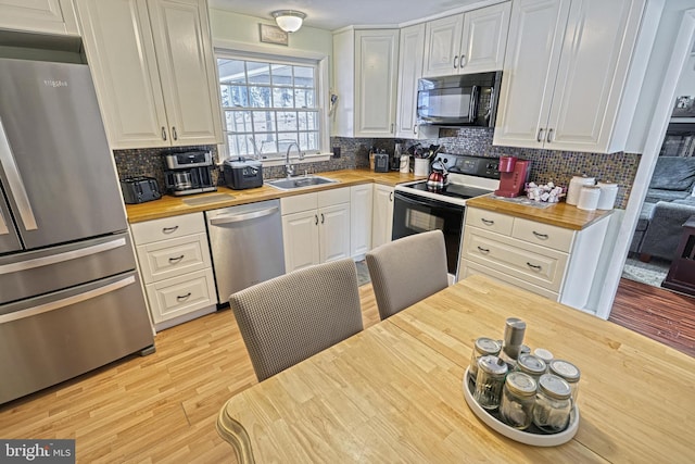 kitchen with sink, butcher block countertops, white cabinetry, light hardwood / wood-style flooring, and appliances with stainless steel finishes