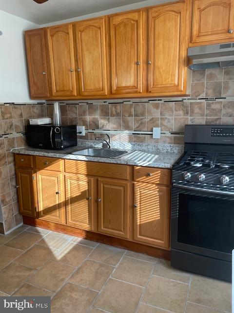 kitchen with tasteful backsplash, sink, light stone counters, and black appliances