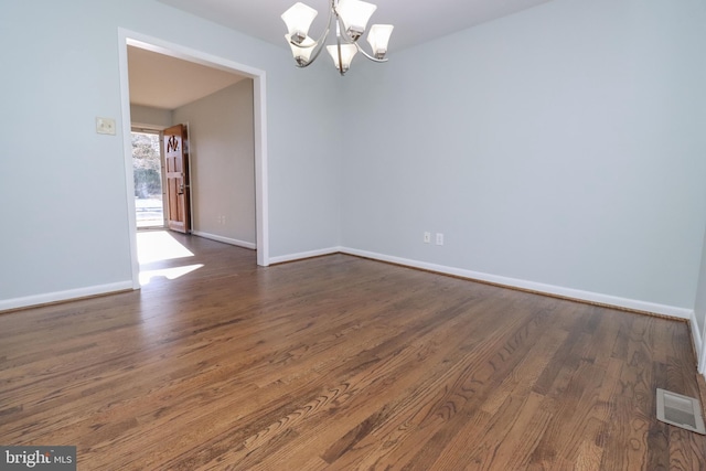 spare room with dark wood-type flooring and an inviting chandelier