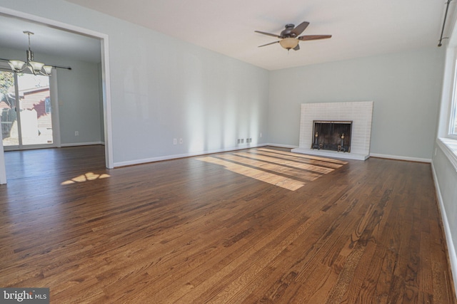 unfurnished living room with dark hardwood / wood-style floors, ceiling fan with notable chandelier, and a brick fireplace