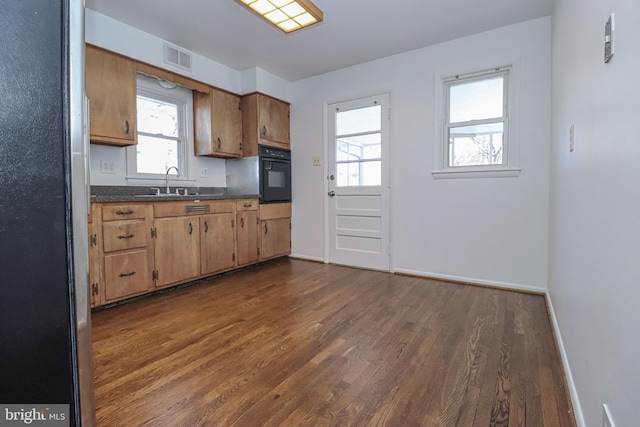 kitchen featuring sink, dark wood-type flooring, black oven, and stainless steel fridge