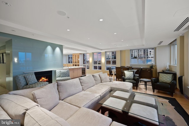 living room with light hardwood / wood-style flooring, beverage cooler, and a raised ceiling