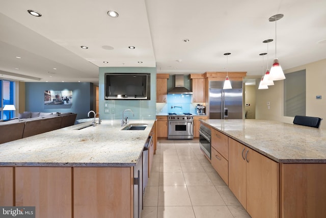 kitchen featuring sink, hanging light fixtures, high end appliances, light stone counters, and wall chimney exhaust hood