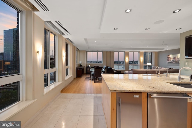 kitchen with light stone countertops, sink, light tile patterned floors, and a kitchen island with sink