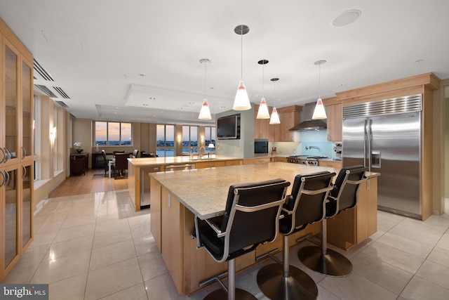 kitchen with wall chimney exhaust hood, stainless steel appliances, a breakfast bar, and a kitchen island