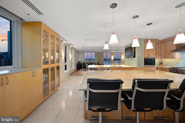 kitchen featuring light tile patterned flooring, a kitchen bar, light stone counters, and hanging light fixtures