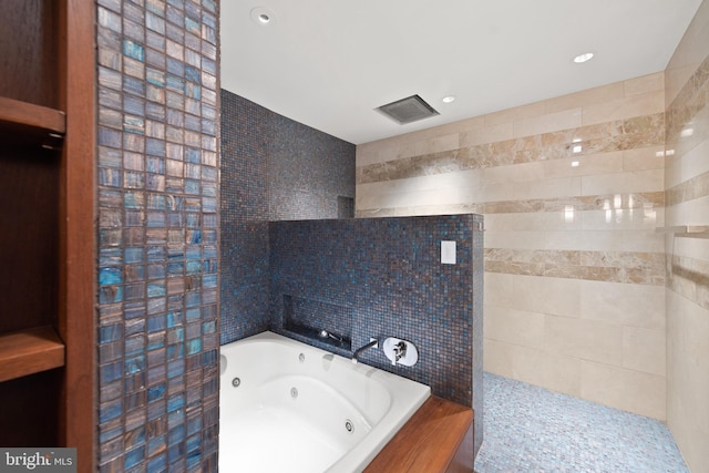 bathroom featuring a relaxing tiled tub and tile walls