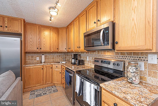 kitchen with appliances with stainless steel finishes, rail lighting, sink, light tile patterned floors, and light stone countertops