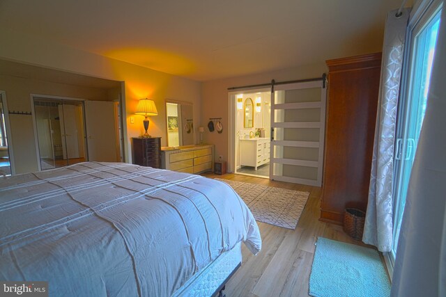 bedroom featuring a barn door, light wood-type flooring, and ensuite bath